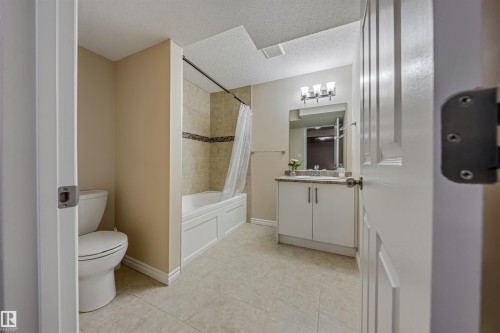 Full bathroom featuring a white panel tub, tiled shower surround with decorative accent, a single vanity with stone-finish countertop, and tiled flooring - 2314 22 Avenue, Edmonton, AB - Indoor Photo Showing Bathroom