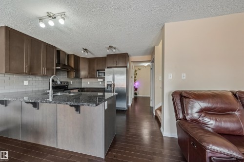 Kitchen featuring dark wood-finish cabinetry, stainless steel appliances, a dark stone island with an undermount sink, and a gray subway tile backsplash - 2314 22 Avenue, Edmonton, AB - Indoor Photo Showing Kitchen