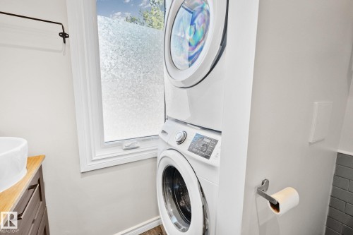 Bathroom featuring a stacked washer and dryer, a window with frosted privacy film, a wood-finish vanity with a vessel sink, and a gray subway tile accent wall - 13635 108 Avenue, Edmonton, AB - Indoor Photo Showing Laundry Room