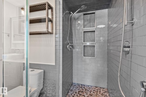 Walk-in shower featuring subway tile, pebble flooring, recessed shelving, and a handheld showerhead - 13635 108 Avenue, Edmonton, AB - Indoor Photo Showing Bathroom