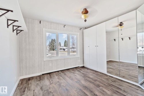 Spacious room featuring wood-finish flooring, a large multi-pane window, and a full wall of mirrored and white panel built-in cabinetry - 13635 108 Avenue, Edmonton, AB - Indoor Photo Showing Other Room