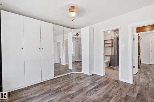 White built-in cabinetry with black hardware, mirrored closet doors, wood-finish flooring, recessed lighting, and a bathroom entry with a glass-enclosed shower - 13635 108 Avenue, Edmonton, AB - Indoor Photo Showing Other Room
