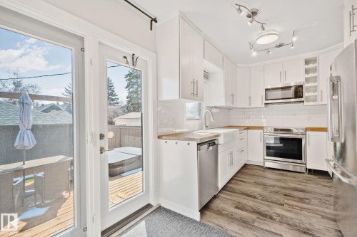 White kitchen cabinetry featuring stainless steel appliances, wood-finish countertops, and wood-finish flooring - 13635 108 Avenue, Edmonton, AB - Indoor Photo Showing Kitchen With Upgraded Kitchen