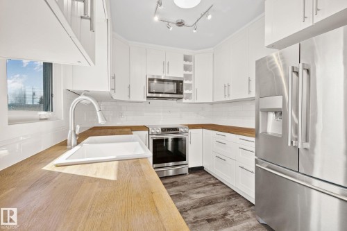 White cabinetry kitchen featuring wood-finish countertops, stainless steel appliances, a white subway tile backsplash, and wood-look flooring - 13635 108 Avenue, Edmonton, AB - Indoor Photo Showing Kitchen With Double Sink With Upgraded Kitchen