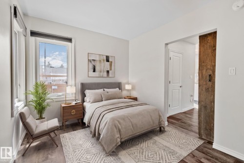 Well-lit bedroom featuring light gray walls, wood-finish flooring, a large window with roller shades, and a rustic wood sliding barn door - 13635 108 Avenue, Edmonton, AB - Indoor Photo Showing Bedroom