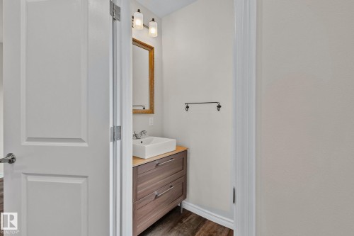 Modern powder room featuring a wood-finish vanity with drawer storage, a vessel sink, and a decorative mirror - 13635 108 Avenue, Edmonton, AB - Indoor Photo Showing Bathroom