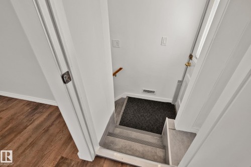 Staircase featuring wood-finish flooring, light grey stair treads, white painted walls, and a white door with brass hardware - 13635 108 Avenue, Edmonton, AB - Indoor Photo Showing Other Room