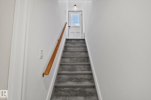 Staircase with wood-finish handrail, light gray wall paint, and door with upper paneled glass - 13635 108 Avenue, Edmonton, AB - Indoor Photo Showing Other Room