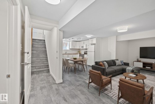 Open-concept living space featuring grey wood-finish flooring, a kitchen with white cabinetry and stainless steel appliances, a dining area, and a carpeted staircase - 13635 108 Avenue, Edmonton, AB - Indoor Photo Showing Living Room