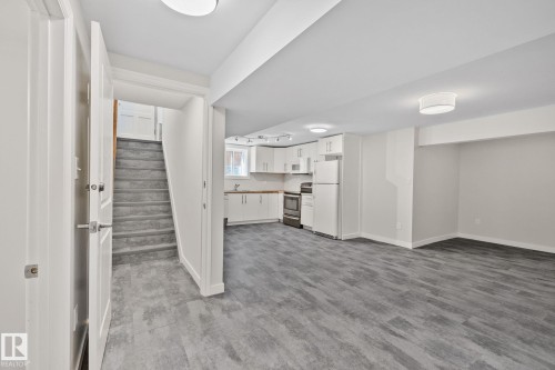 Open-concept lower level featuring wood-finish flooring, a full kitchen with white cabinetry and stainless steel appliances, and recessed lighting - 13635 108 Avenue, Edmonton, AB - Indoor Photo Showing Other Room