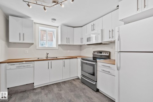 Modern kitchen featuring white cabinetry with brushed nickel hardware, wood-finish countertops, stainless steel appliances, and wood-finish flooring - 13635 108 Avenue, Edmonton, AB - Indoor Photo Showing Kitchen With Double Sink