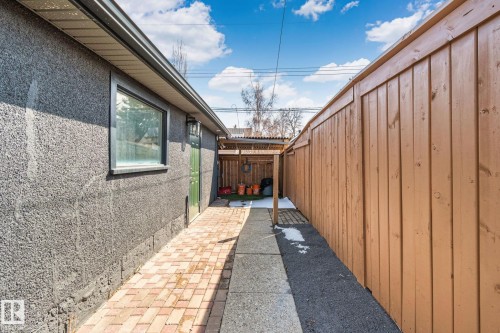 Side yard featuring a textured stucco exterior, a wood privacy fence, and a brick-paved walkway leading to a rear entrance - 13635 108 Avenue, Edmonton, AB - Outdoor With Exterior