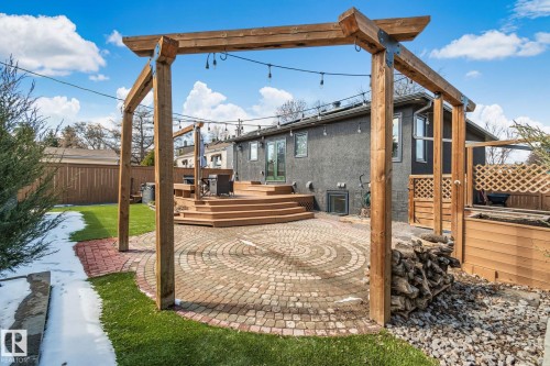 Expansive outdoor living area featuring a multi-level wood deck, a circular paver patio, a wooden pergola, and a stone-lined garden bed - 13635 108 Avenue, Edmonton, AB - Outdoor