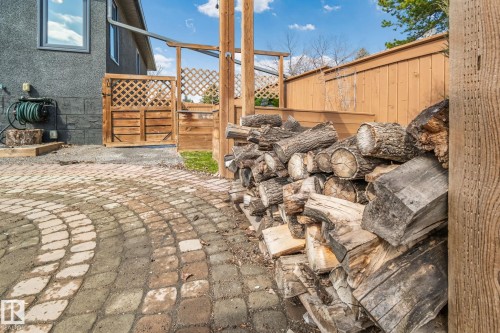 Paver stone patio featuring a circular pattern, alongside a stacked woodpile, wood lattice fencing, and a side exterior with stucco finish - 13635 108 Avenue, Edmonton, AB - Outdoor With Deck Patio Veranda