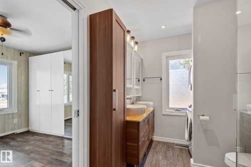Bathroom featuring a dual vessel sink vanity with wood-finish countertop, wood-finish flooring, a white window with frosted glass, and a glass-enclosed shower - 13635 108 Avenue, Edmonton, AB - Indoor Photo Showing Other Room