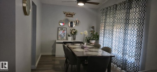 Dining area featuring wood-look flooring, a ceiling fan with integrated lighting, and a large window with patterned curtains - 5420 40 Avenue, Wetaskiwin, AB - Indoor Photo Showing Dining Room