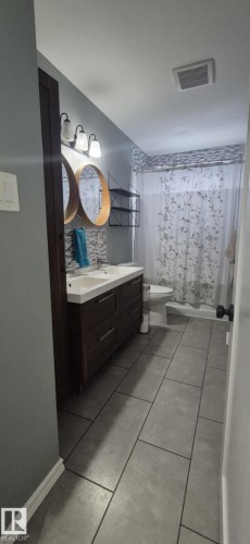 Bathroom featuring a double vanity with two sinks, two circular mirrors, and a shower with a curtain - 5420 40 Avenue, Wetaskiwin, AB - Indoor Photo Showing Bathroom