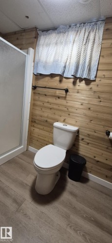 Bathroom featuring wood paneled walls, a white toilet, and light-colored plank flooring - 5420 40 Avenue, Wetaskiwin, AB - Indoor Photo Showing Bathroom