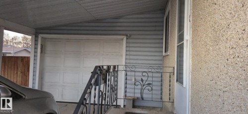 The property includes a carport with a white garage door, light grey siding, and a decorative wrought iron railing on the porch - 5420 40 Avenue, Wetaskiwin, AB -  With Exterior