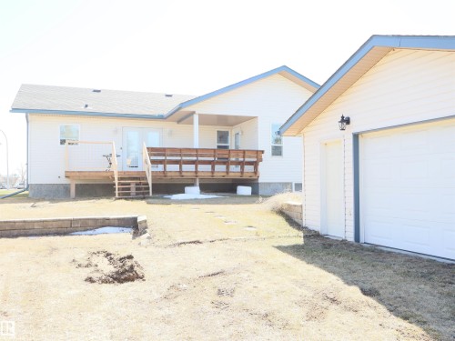 Rear exterior featuring a spacious wood deck with steps, an adjacent covered porch, and a detached two-car garage - 5802 52 Avenue, Barrhead, AB - Outdoor