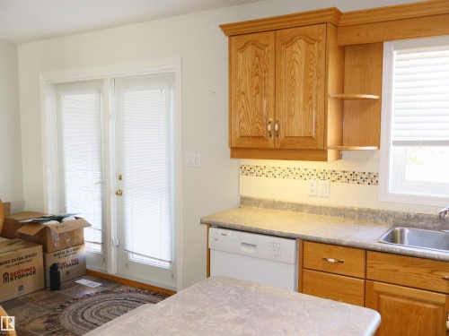 Kitchen area featuring wood-finish cabinetry, a stainless steel sink, a built-in dishwasher, and a decorative tile backsplash - 5802 52 Avenue, Barrhead, AB - Indoor