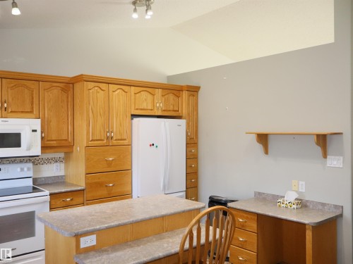 Kitchen featuring extensive wood cabinetry, white appliances, a peninsula with seating space, and a built-in desk area - 5802 52 Avenue, Barrhead, AB - Indoor Photo Showing Kitchen