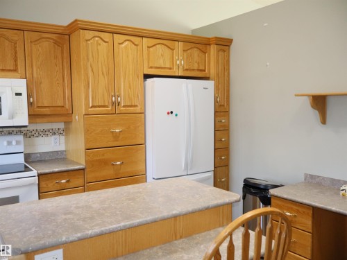 Kitchen featuring wood-finish cabinetry with crown molding, a tiled backsplash, and light-toned countertops - 5802 52 Avenue, Barrhead, AB - Indoor Photo Showing Kitchen