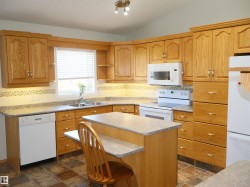 Kitchen featuring extensive wood cabinetry, a central island with a breakfast bar, white appliances, and tiled flooring - 