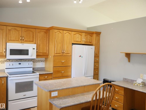 Full kitchen featuring wood cabinetry, white appliances, a patterned tile backsplash, laminate countertops, and vaulted ceilings - 5802 52 Avenue, Barrhead, AB - Indoor Photo Showing Kitchen