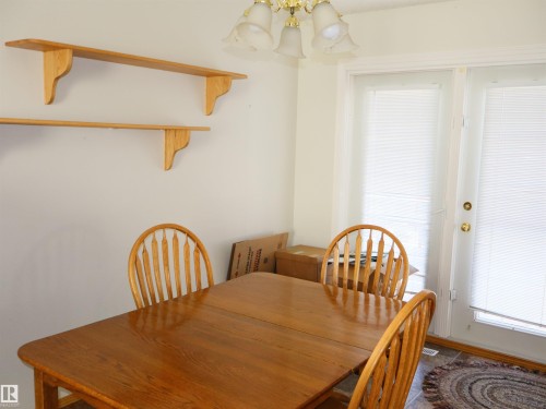 Bright room featuring a pair of double patio doors with integrated blinds, overhead ceiling light fixture, two wall-mounted wooden shelves, and tile flooring - 5802 52 Avenue, Barrhead, AB - Indoor Photo Showing Dining Room