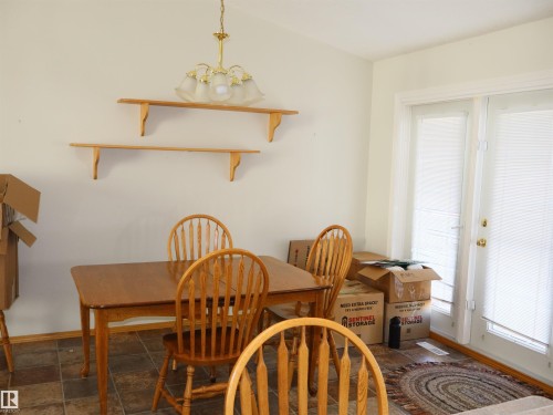 Tiled flooring throughout this space, featuring a brass chandelier, two wall-mounted wooden shelves, and double glass-paned doors with white blinds - 5802 52 Avenue, Barrhead, AB - Indoor Photo Showing Dining Room