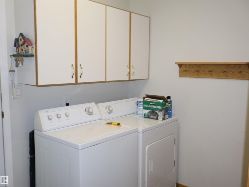 Functional laundry area featuring white upper cabinetry with wood-finish trim, a wood-finish wall shelf with pegs, and light-toned walls - 5802 52 Avenue, Barrhead, AB - Indoor Photo Showing Laundry Room