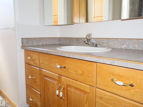 Bathroom vanity featuring a wood-finish cabinet, integrated sink, and laminate countertop - 5802 52 Avenue, Barrhead, AB - Indoor Photo Showing Bathroom