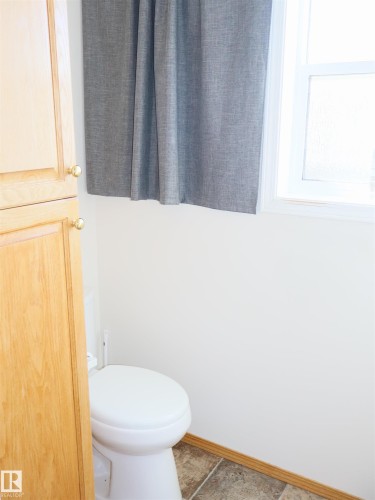 White toilet with light wood-finish cabinetry featuring brass-tone hardware - 5802 52 Avenue, Barrhead, AB - Indoor Photo Showing Bathroom