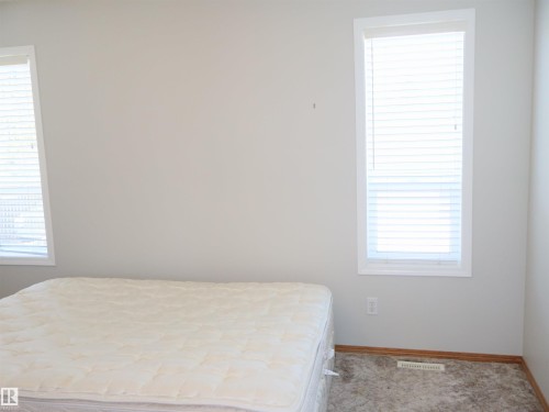 Room with light gray walls, two windows with white blinds, and gray carpet flooring - 5802 52 Avenue, Barrhead, AB - Indoor Photo Showing Bedroom