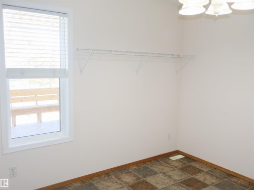 Room featuring a window with blinds, wire shelving, a ceiling-mounted light fixture, and patterned floor tiling with wood-finish baseboards - 5802 52 Avenue, Barrhead, AB - Indoor Photo Showing Other Room