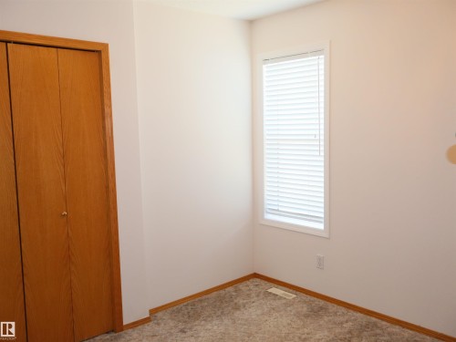 Bedroom featuring light carpeting, white walls, wood-finish bi-fold closet doors, and a window with blinds - 5802 52 Avenue, Barrhead, AB - Indoor Photo Showing Other Room