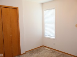 Bedroom featuring light carpeting, white walls, wood-finish bi-fold closet doors, and a window with blinds - 