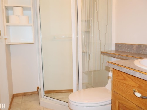 Bathroom featuring a glass-enclosed shower, built-in shelving, wood-finish vanity, and a laminate countertop with an integrated sink - 5802 52 Avenue, Barrhead, AB - Indoor Photo Showing Bathroom