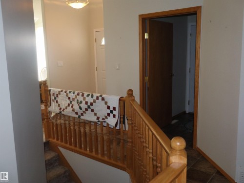 Natural wood banister and railing with a paneled door and light-toned walls - 5802 52 Avenue, Barrhead, AB - Indoor Photo Showing Other Room