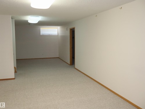 Spacious room with light-colored carpet flooring, white painted walls, and wood trim - 5802 52 Avenue, Barrhead, AB - Indoor Photo Showing Other Room