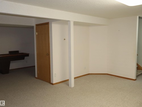 Open finished space featuring light-toned carpet flooring, light-colored walls, and wood trim - 5802 52 Avenue, Barrhead, AB - Indoor Photo Showing Other Room