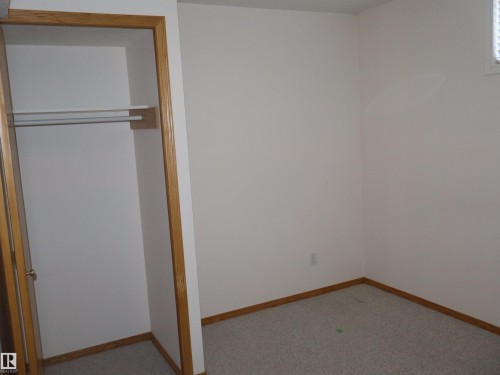 Carpeted interior space featuring a built-in closet with natural wood trim, white walls, and a window with horizontal blinds - 5802 52 Avenue, Barrhead, AB - Indoor Photo Showing Other Room