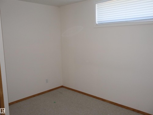 Carpeted room featuring light-colored walls, wood-finish baseboards, and a single window with horizontal blinds - 5802 52 Avenue, Barrhead, AB - Indoor Photo Showing Other Room
