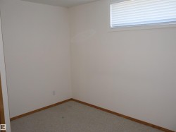 Carpeted room featuring light-colored walls, wood-finish baseboards, and a single window with horizontal blinds - 