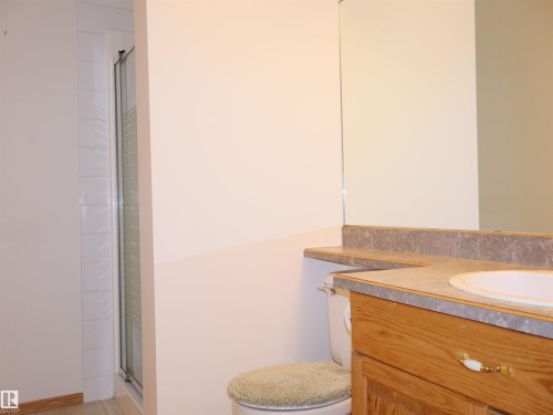 Bathroom vanity featuring a light wood-finish cabinet with a single basin sink, a stone-look countertop, and a large wall-mounted mirror - 5802 52 Avenue, Barrhead, AB - Indoor Photo Showing Bathroom