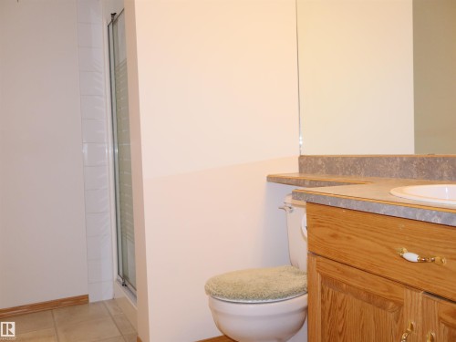 Bathroom featuring a wood-finish vanity with a laminate countertop, integrated sink, and a large wall-mounted mirror - 5802 52 Avenue, Barrhead, AB - Indoor Photo Showing Bathroom