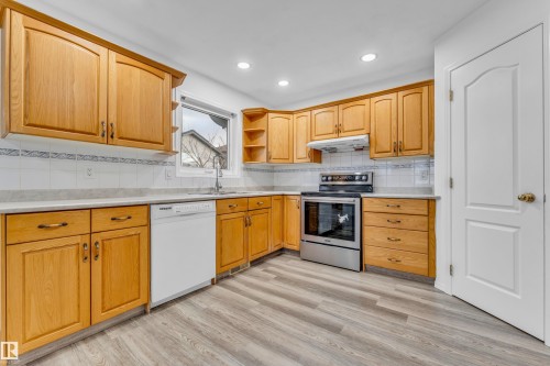 Kitchen featuring ample wood cabinetry, light grey countertops, a white tile backsplash with decorative accent, stainless steel range, and wood-finish flooring - 4103 37A Avenue, Edmonton, AB - Indoor Photo Showing Kitchen