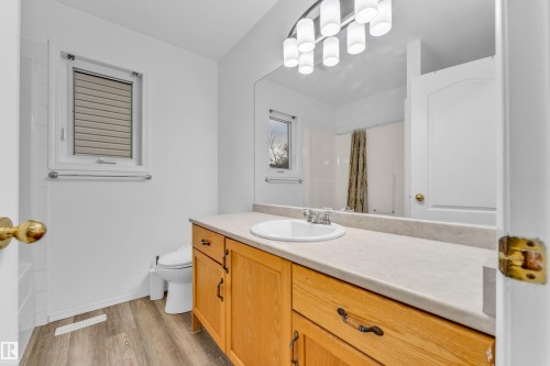 Bathroom featuring wood-finish flooring, a wood-finish vanity with a light-toned countertop, a single sink, an overhead mirror, and a wall-mounted light fixture - 4103 37A Avenue, Edmonton, AB - Indoor Photo Showing Bathroom