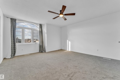 Spacious room featuring a large arched window, light gray carpeting, and a wood-finish ceiling fan with integrated lighting - 4103 37A Avenue, Edmonton, AB - Indoor Photo Showing Other Room